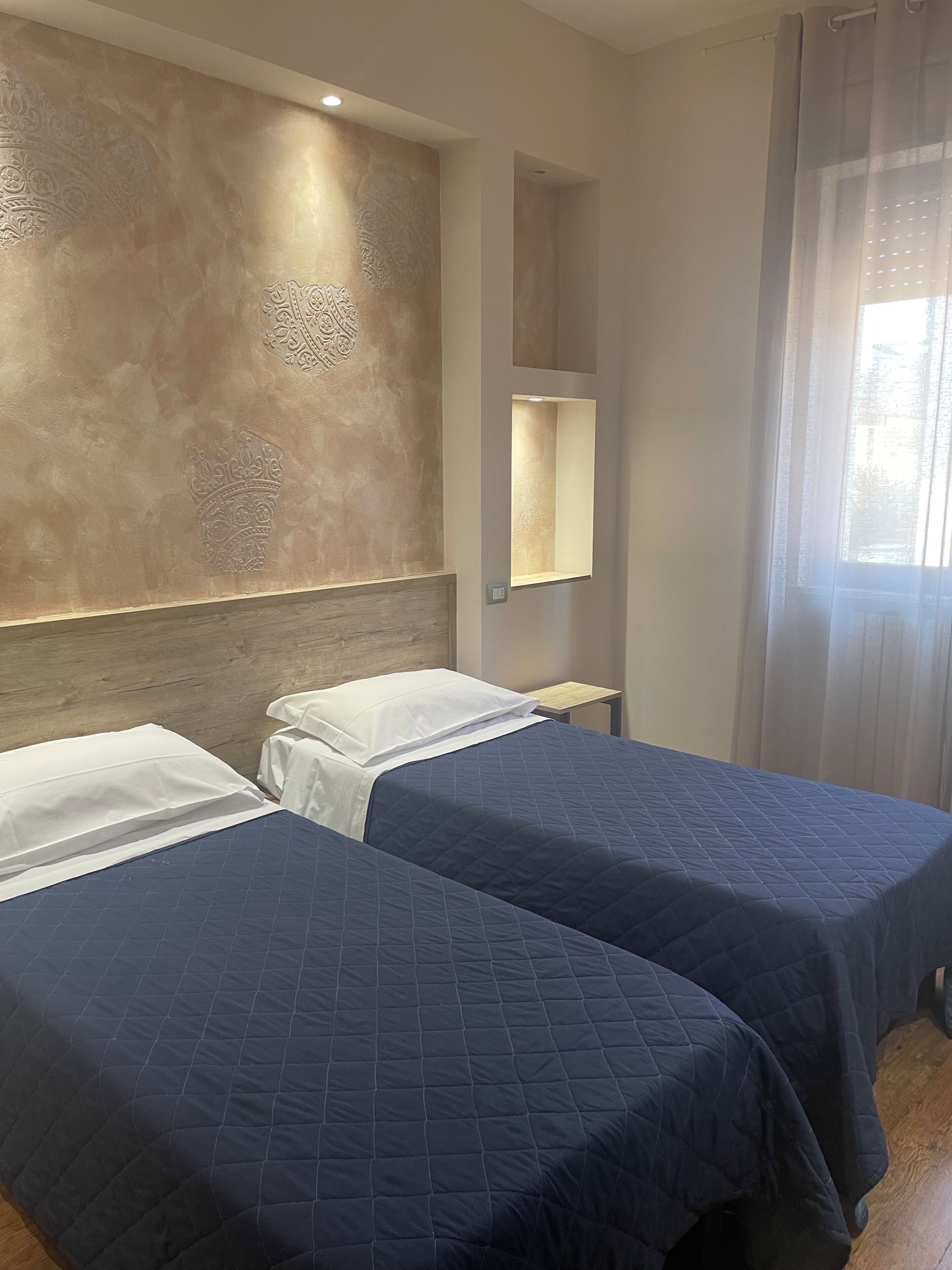 A hotel room with two beds, a wooden headboard, a wall-mounted mirror, and a window with curtains.