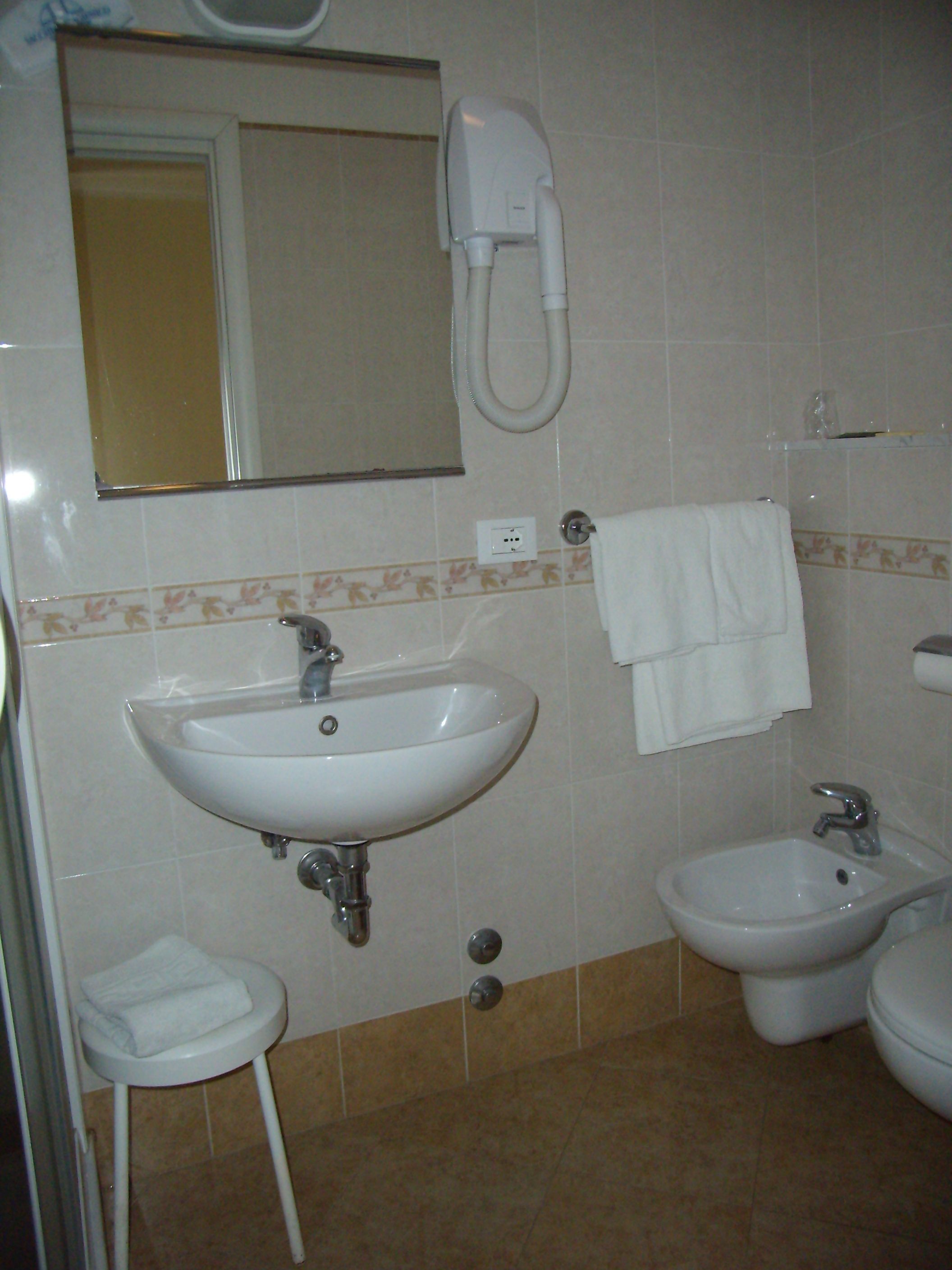 Un baño con lavamanos, bidé y un taburete pequeño.