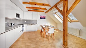 A modern kitchen with white cabinets, a wooden dining table, and a skylight. - DownTown Suites Kodanská (Prague)