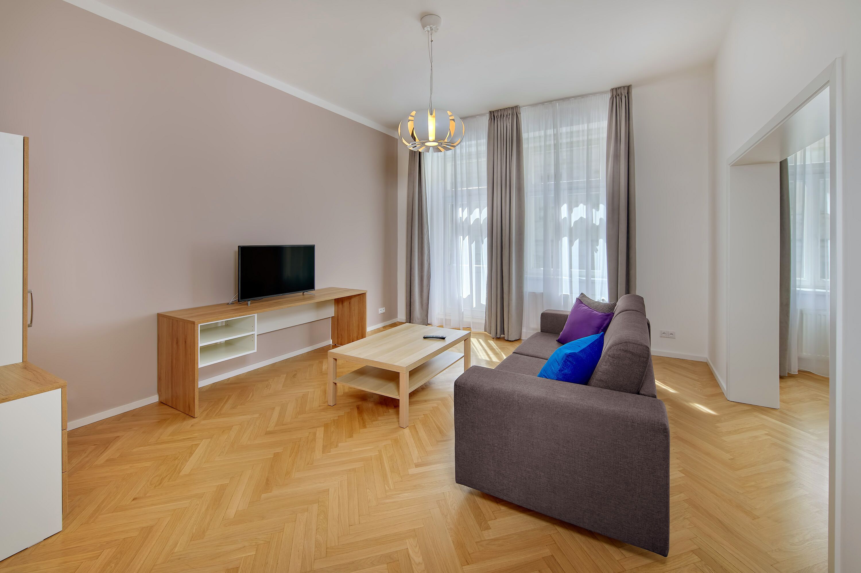 Una sala de estar moderna con un sofá, televisión, mesa de centro de madera y una lámpara colgante.