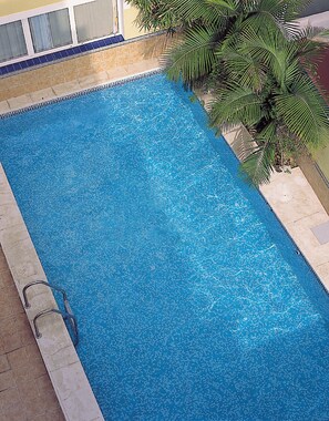 Una piscina rettangolare con bordo piastrellato, una scala sul lato sinistro e una palma sullo sfondo.