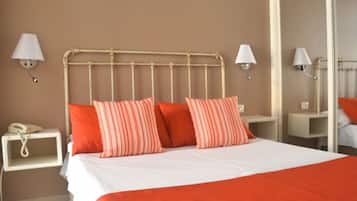 A hotel room with a bed, two bedside lamps, a nightstand with a phone, and a mirror.