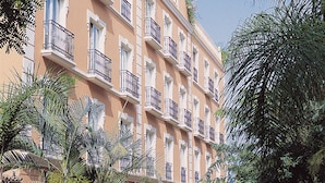Un immeuble à plusieurs étages doté de balcons, entouré de palmiers et bordé par un marché de rue.