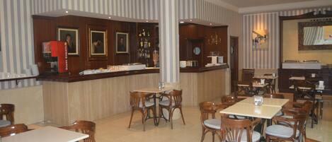 A hotel lobby with striped walls, a bar area with a counter and bar stools, and multiple dining tables and chairs.