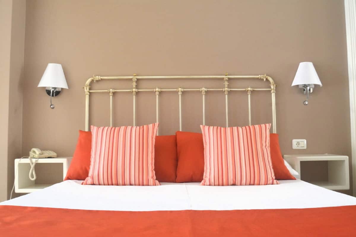 Una cama con cabecera de metal, dos mesitas de noche y dos lámparas de pared.