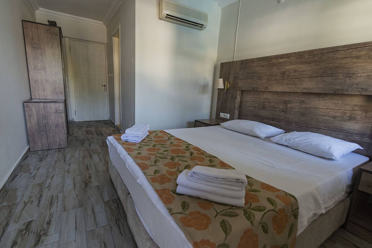 A hotel room with a bed, a nightstand, a wooden headboard, a wardrobe, and an air conditioning unit.