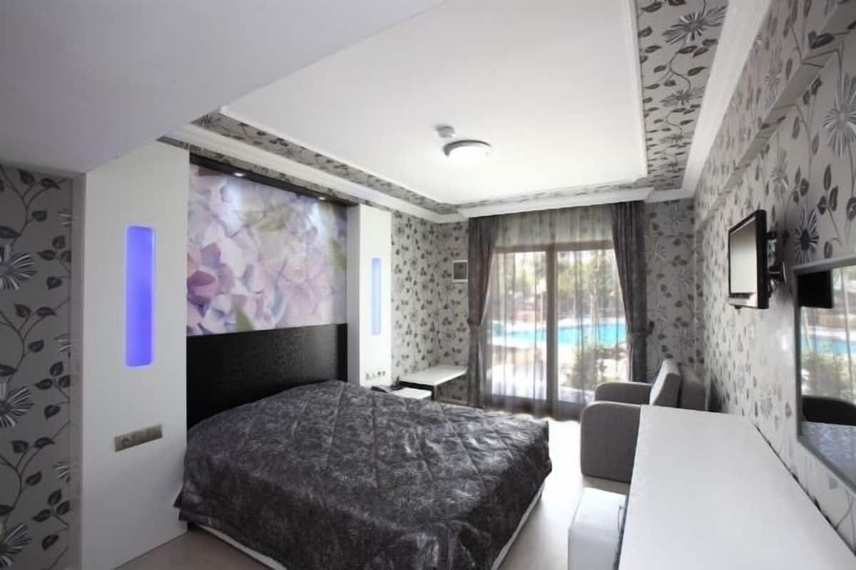 A bedroom with a bed, a desk, and a chair. There is a window with a view of a pool and a balcony.