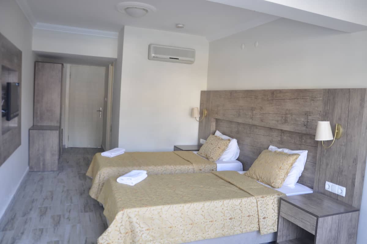 A hotel room with two beds, a wooden headboard, a wall-mounted air conditioner, and a bedside lamp.