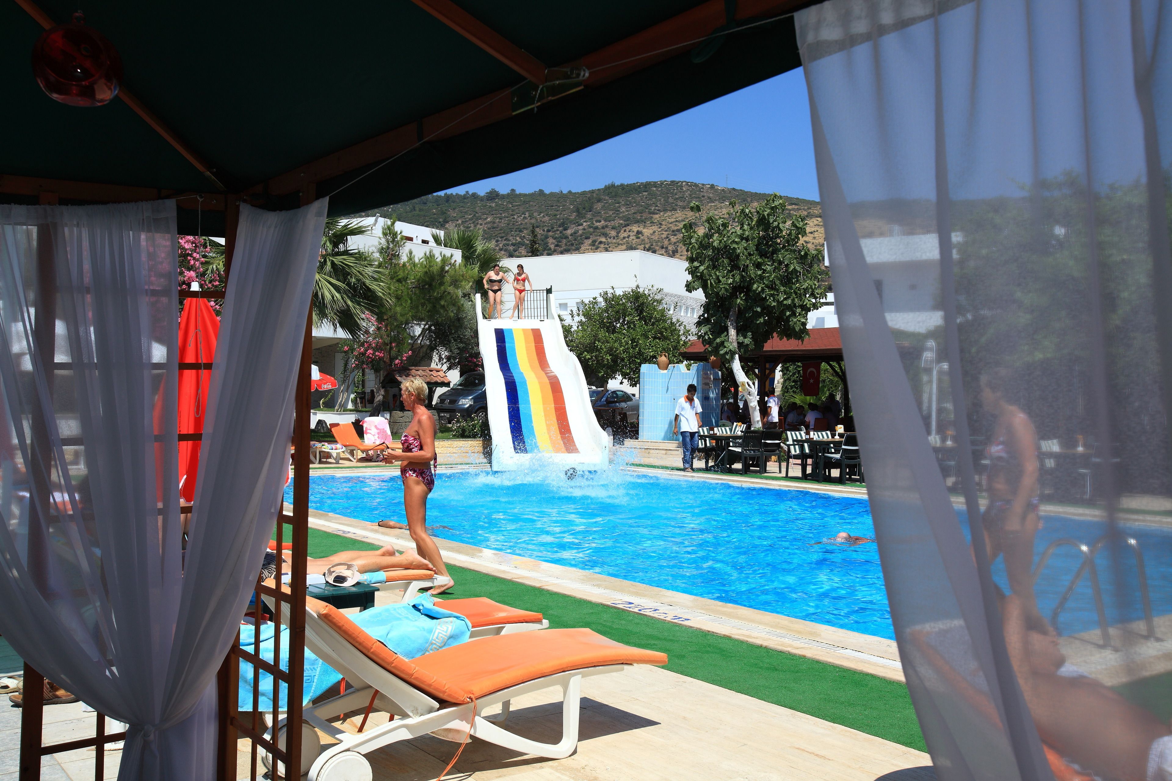Un área de piscina con tobogán, sillas de descanso y vista a una colina.