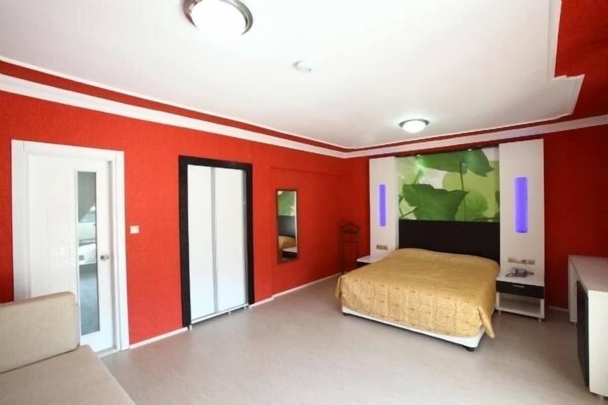 A bedroom with a bed, a wardrobe, a mirror, and a wall with a green leaf design.