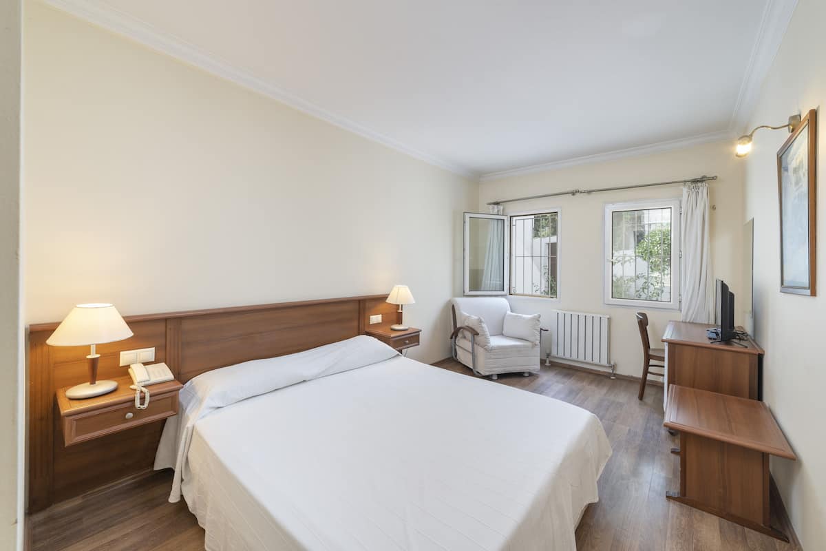 A hotel room with a large bed, bedside lamps, a desk, a chair, and a window with curtains.