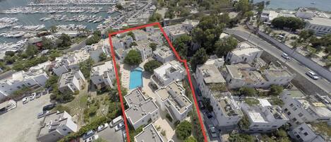 An aerial view of a coastal residential area with a marina, houses, and a swimming pool.