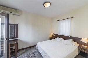 Una habitación de hotel con cama, mesitas de noche, escritorio, silla, ventana con cortinas e iluminación en el techo.