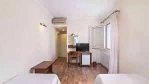 Habitación de hotel con dos camas, un escritorio con televisor, un refrigerador pequeño y una ventana con cortinas.
