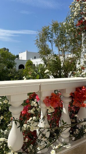 Una balaustrada blanca con flores rojas y blancas, un edificio blanco al fondo y árboles verdes.