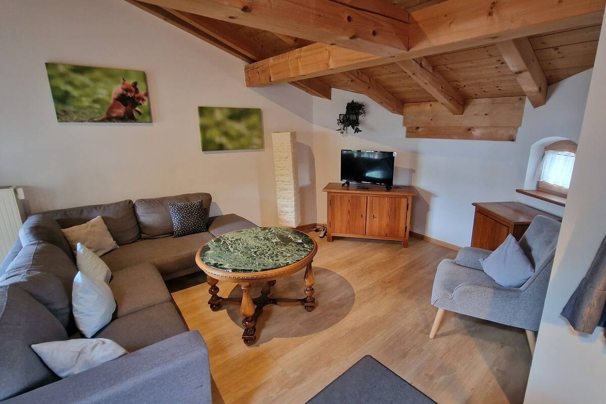 A living room with a wooden ceiling, a grey sofa, a round coffee table, and a television on a wooden cabinet.