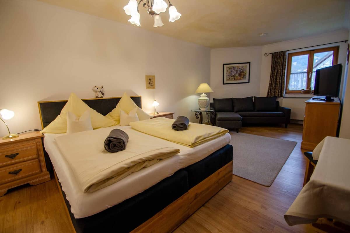 A bedroom with a bed, bedside tables, a sofa, a television, and a window with curtains.