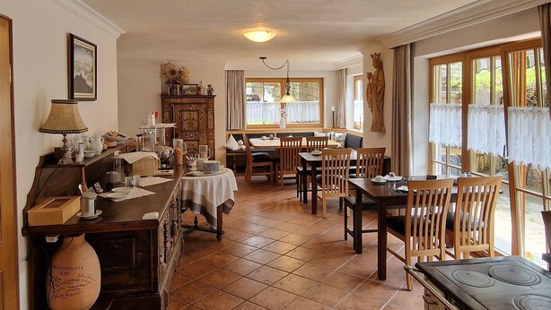 A spacious living area with a dining table, chairs, a fireplace, and a kitchen area with a stove. - Ferienhaus Fux Hotel Garni (Oberammergau)