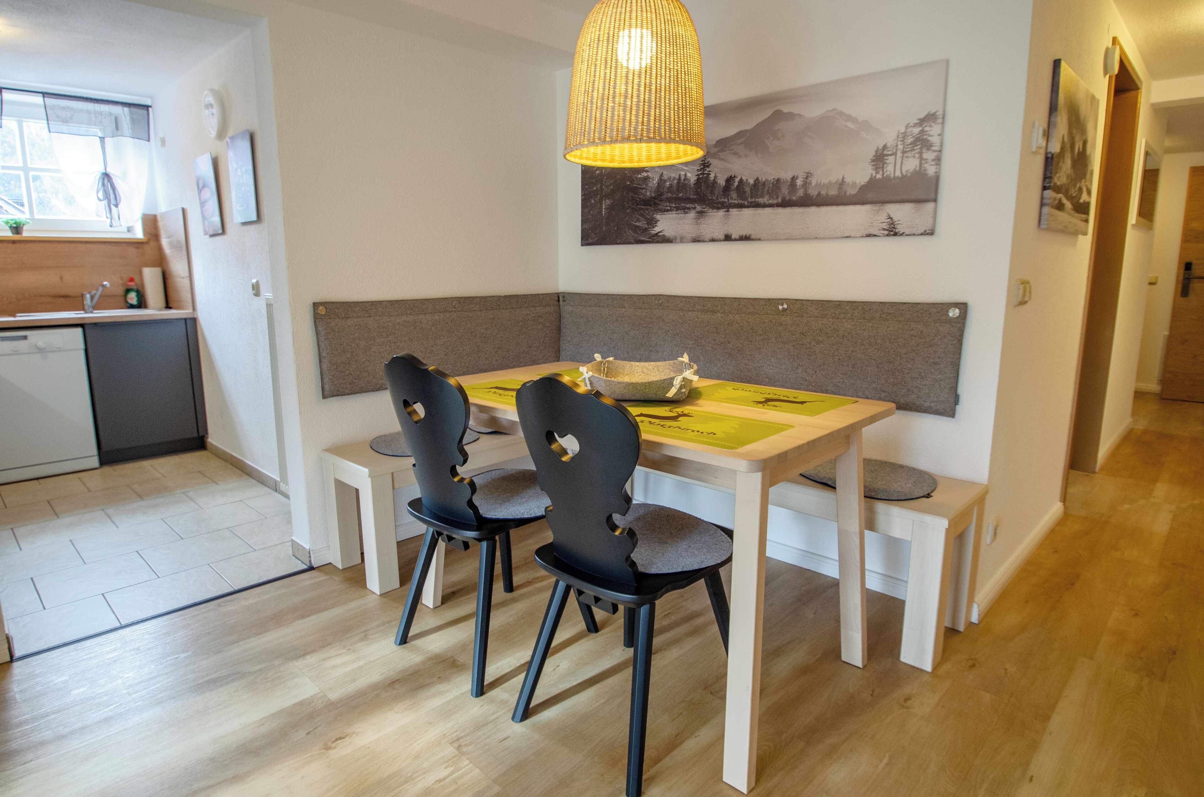 A dining area with a wooden table, two chairs, a bench, and a hanging light fixture.