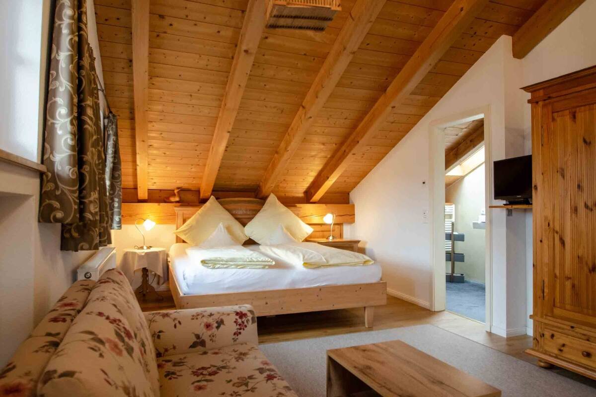A cozy room with a wooden ceiling, a bed with pillows, a wooden cabinet, and a television on a shelf.