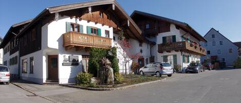 Un hotel europeo tradicional con balcón de madera, una fuente y coches aparcados.