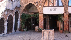 Une cour avec une fontaine en pierre, des portes en arc de cercle et une enseigne indiquant « CAMPELLO DEL REMER ».