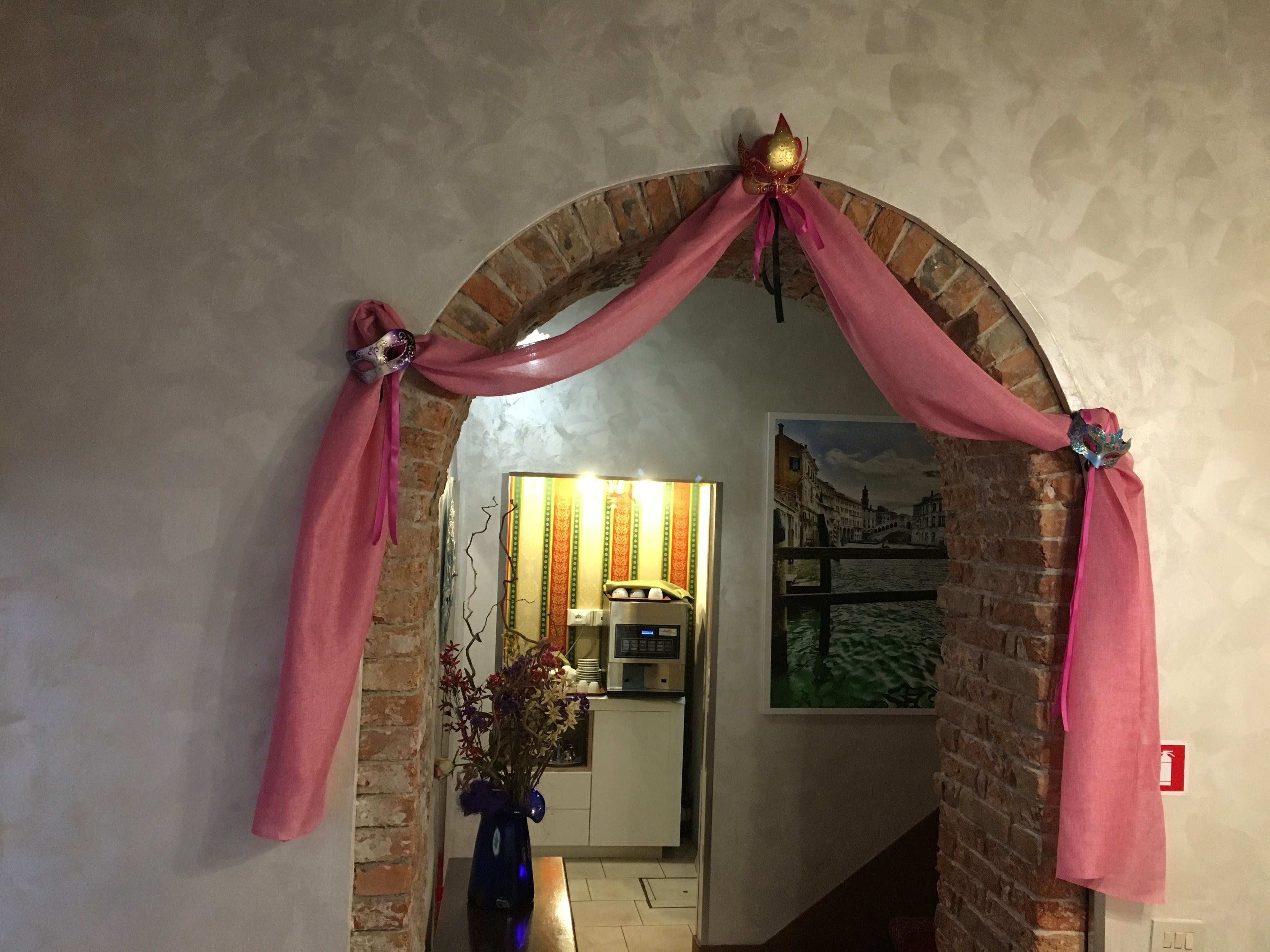 An archway with pink drapes and a golden mask decoration.