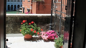 Une cour avec un bâtiment rouge, une grille en fer forgé et des plantes en pot ornées de fleurs roses.