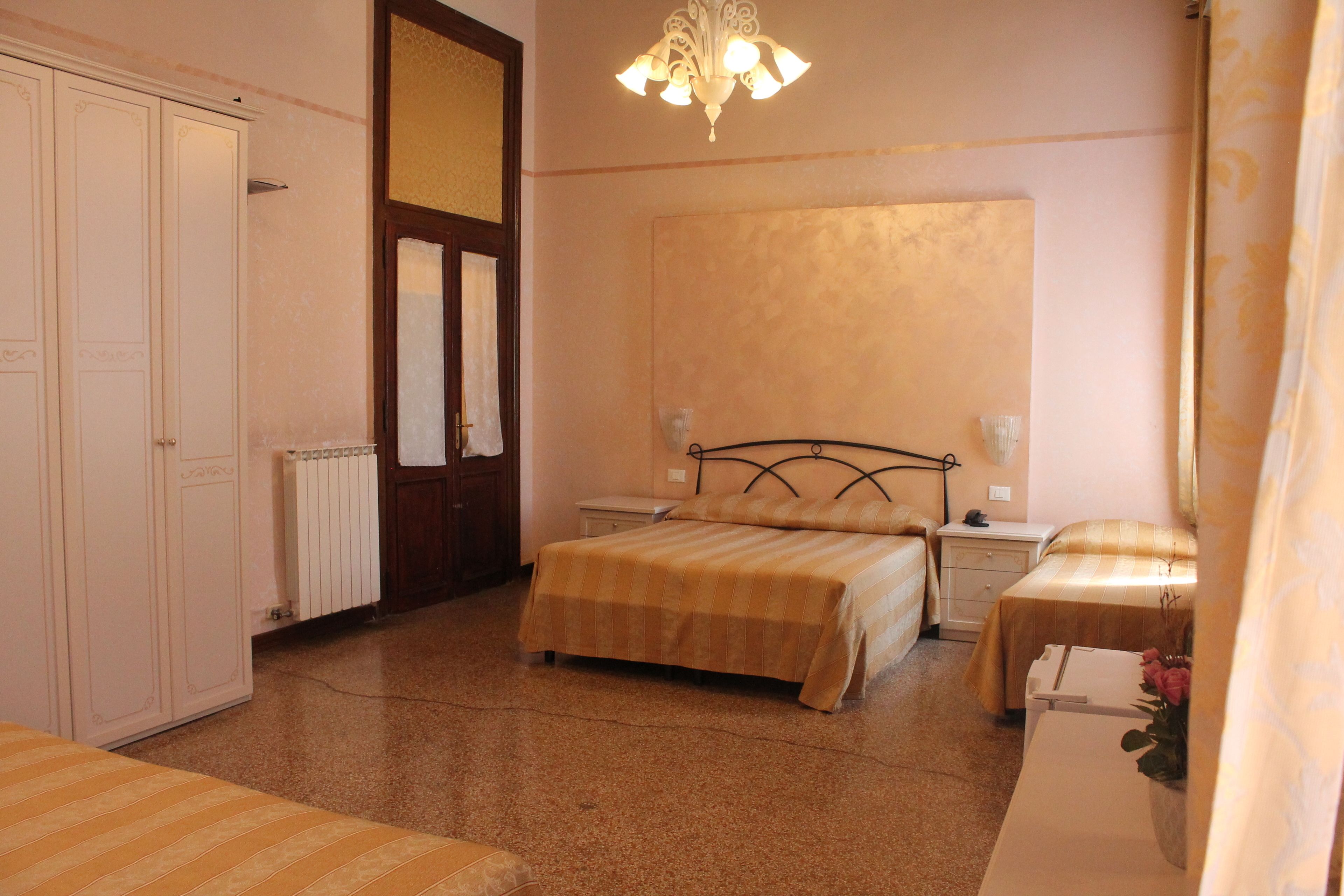 A bedroom with two beds, a wardrobe, a radiator, a nightstand, and a chandelier.