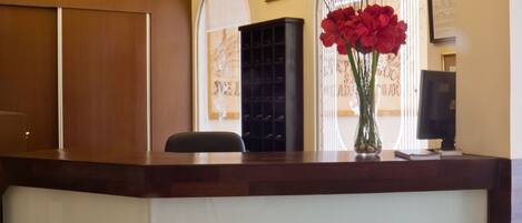 Un mostrador de recepción con un jarrón de flores rojas, una silla negra y un armario de madera.