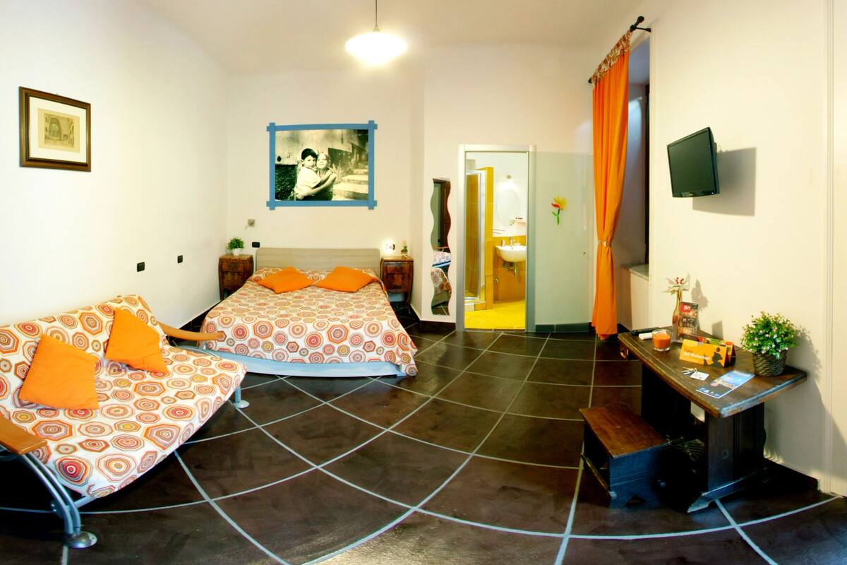 Ein Zimmer mit zwei Betten, einem kleinen Tisch mit Pflanze, einem Fernseher und einem durch eine Tür sichtbaren Badezimmer.