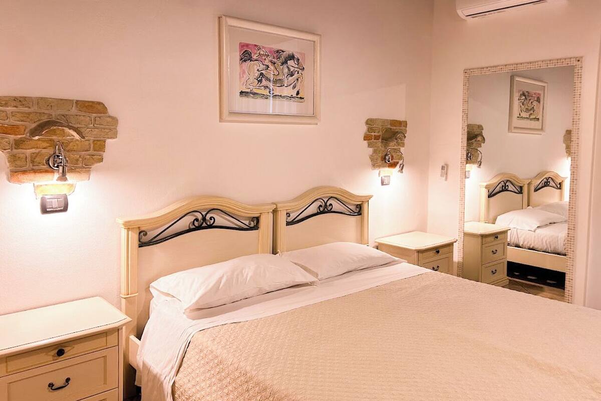 A bedroom with a bed, bedside tables, a mirror, and wall-mounted lights.