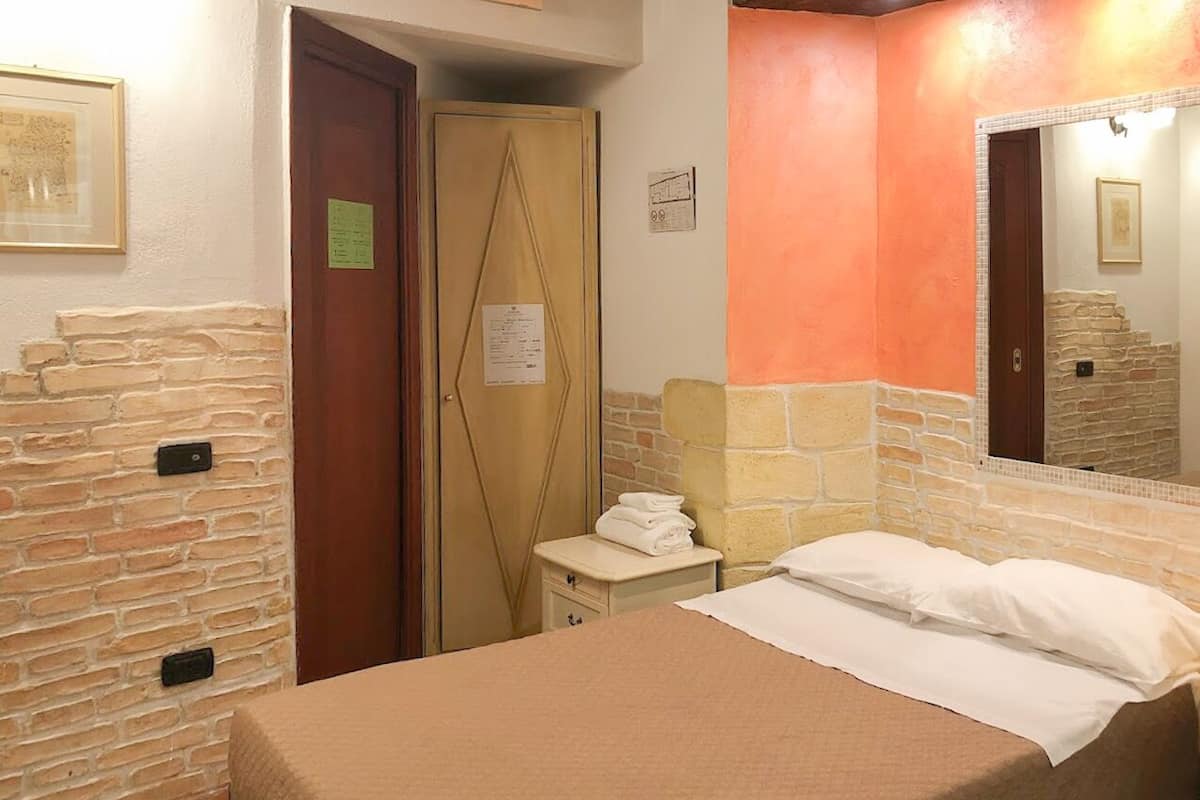 A hotel room with a bed, a nightstand, a mirror, and a door.