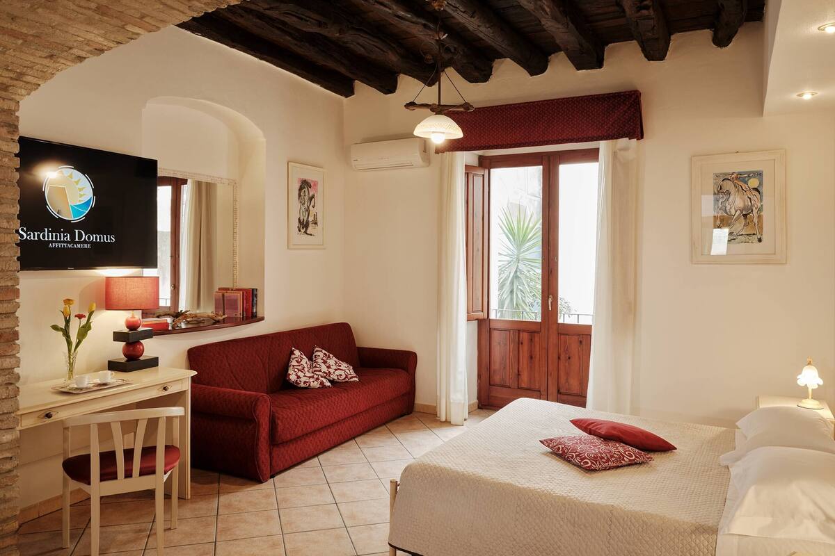A cozy room with a bed, a red sofa, a desk with a chair, a TV, and artwork on the walls.