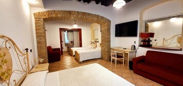 Una camera d'albergo con un letto, una scrivania, un divano rosso e una televisione.