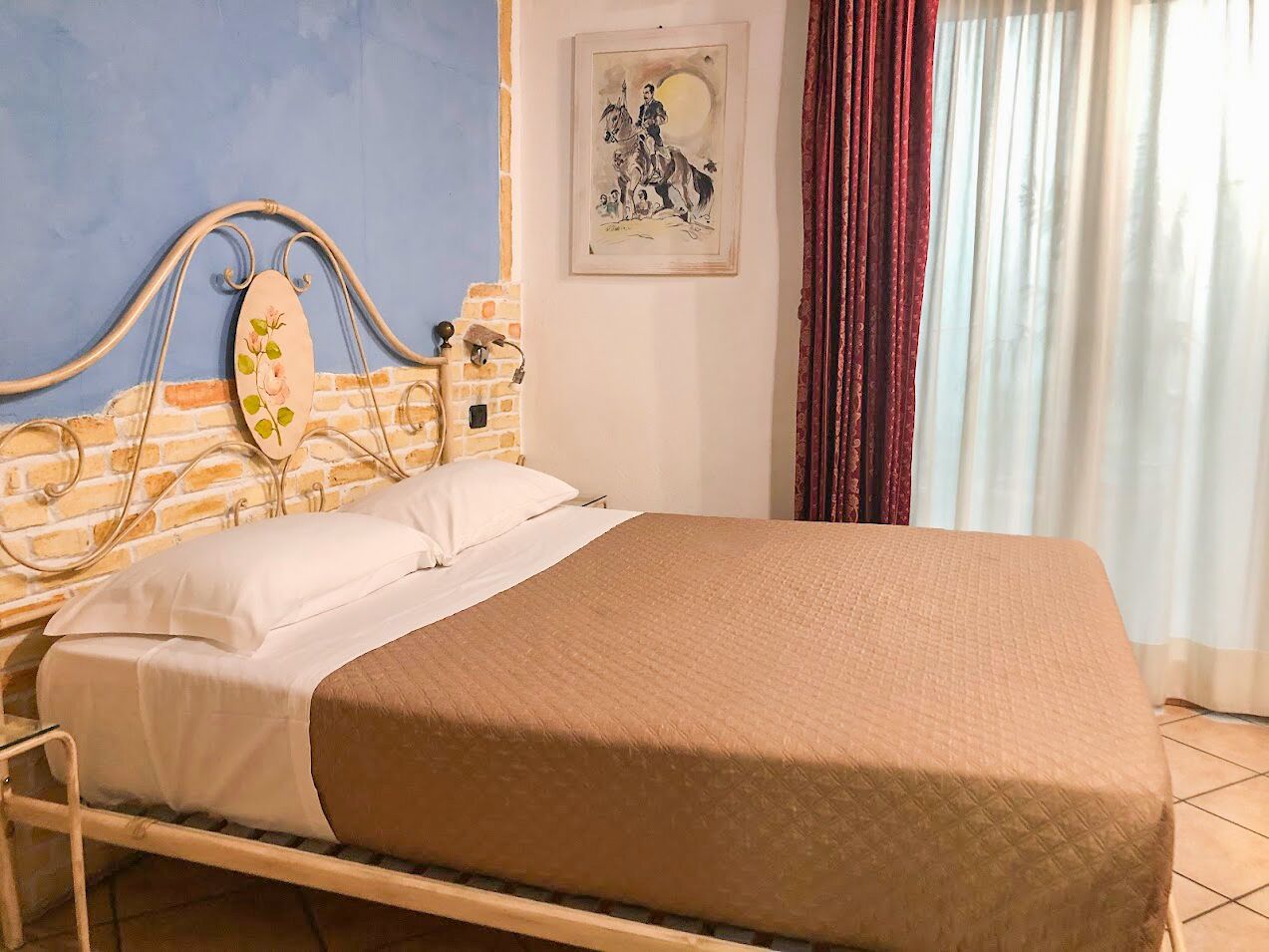 Una cama con cubrecama blanco y marrón, una pared de ladrillo, un cabecero de madera y un cuadro en la pared.