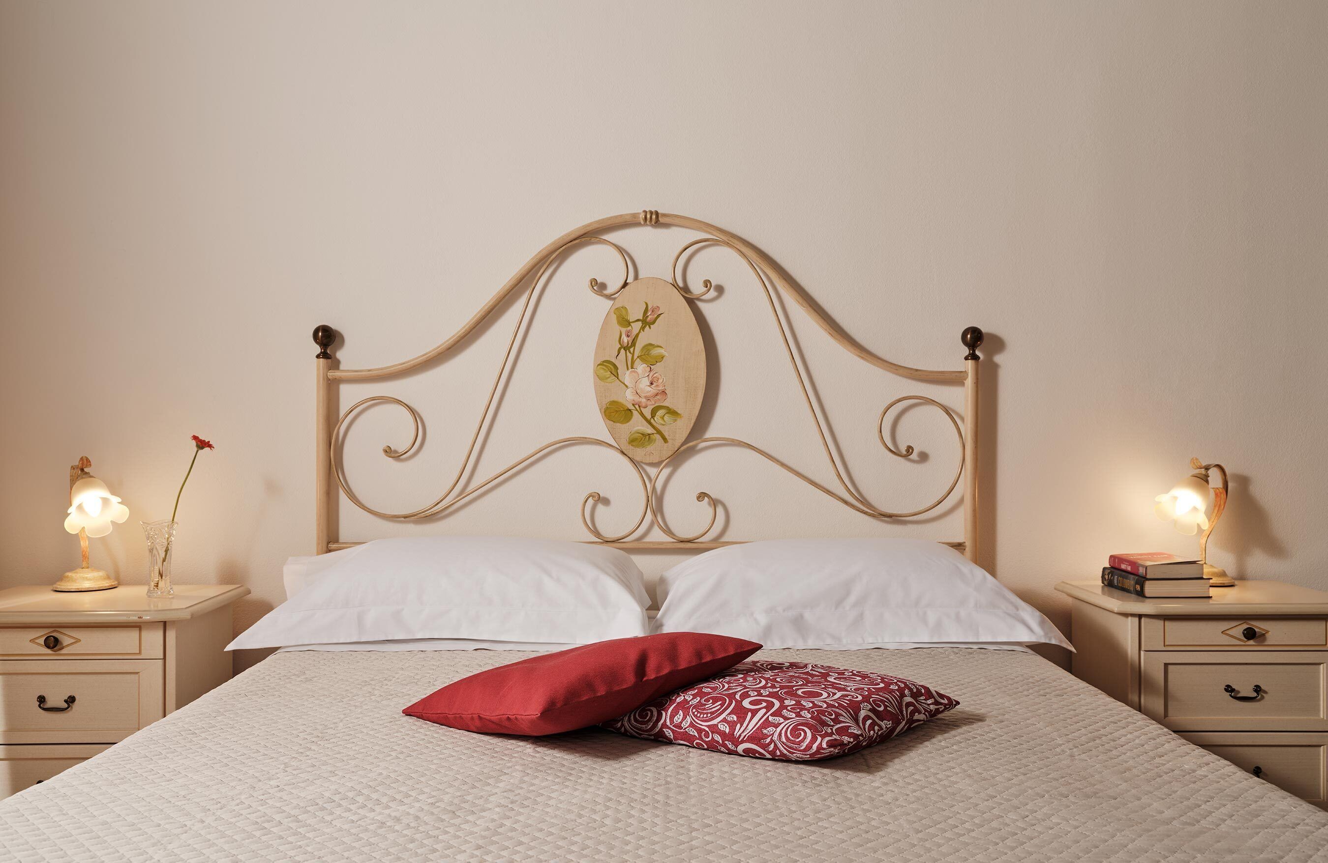Un lit bien fait, avec deux oreillers, une lampe de chevet et une table de nuit sur laquelle se trouvent un livre et un vase.