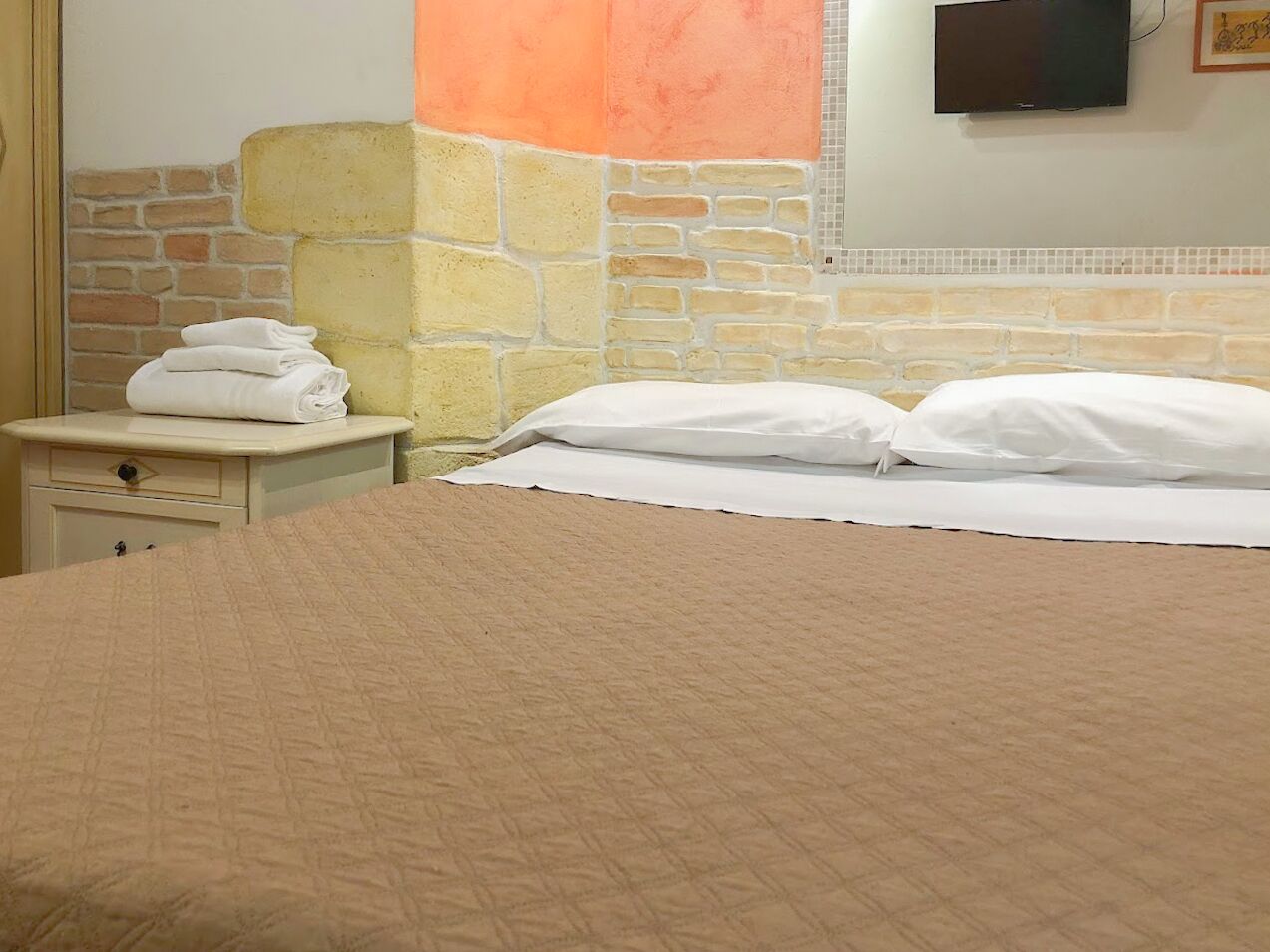 A hotel room with a bed, a nightstand, and a television on the wall.