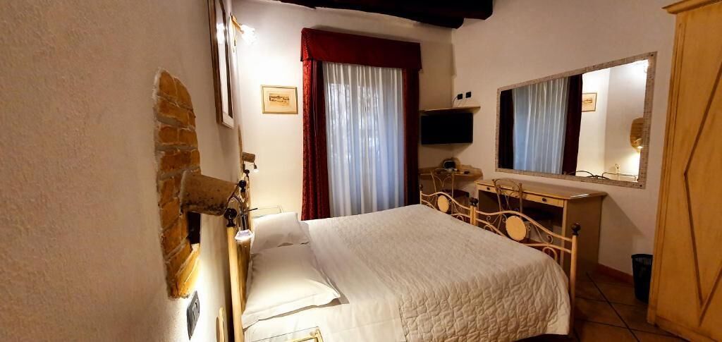 A bedroom with a bed, a wooden dresser, a mirror, and a window with curtains.