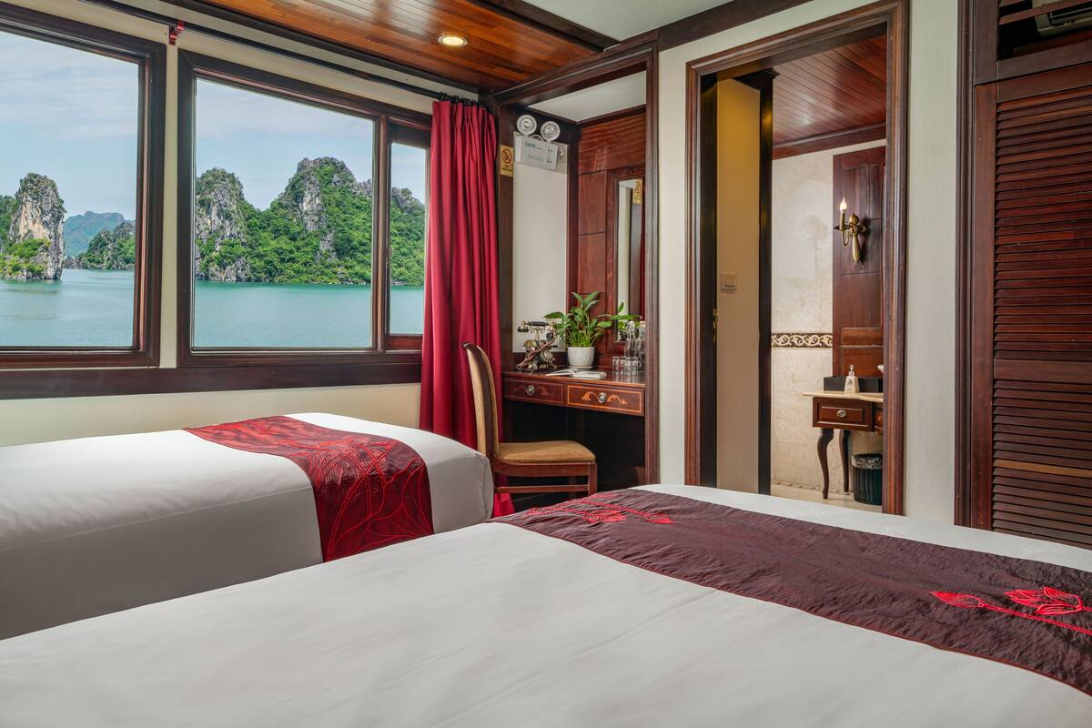 A hotel room with two beds, a desk, and a view of a lake with cliffs.