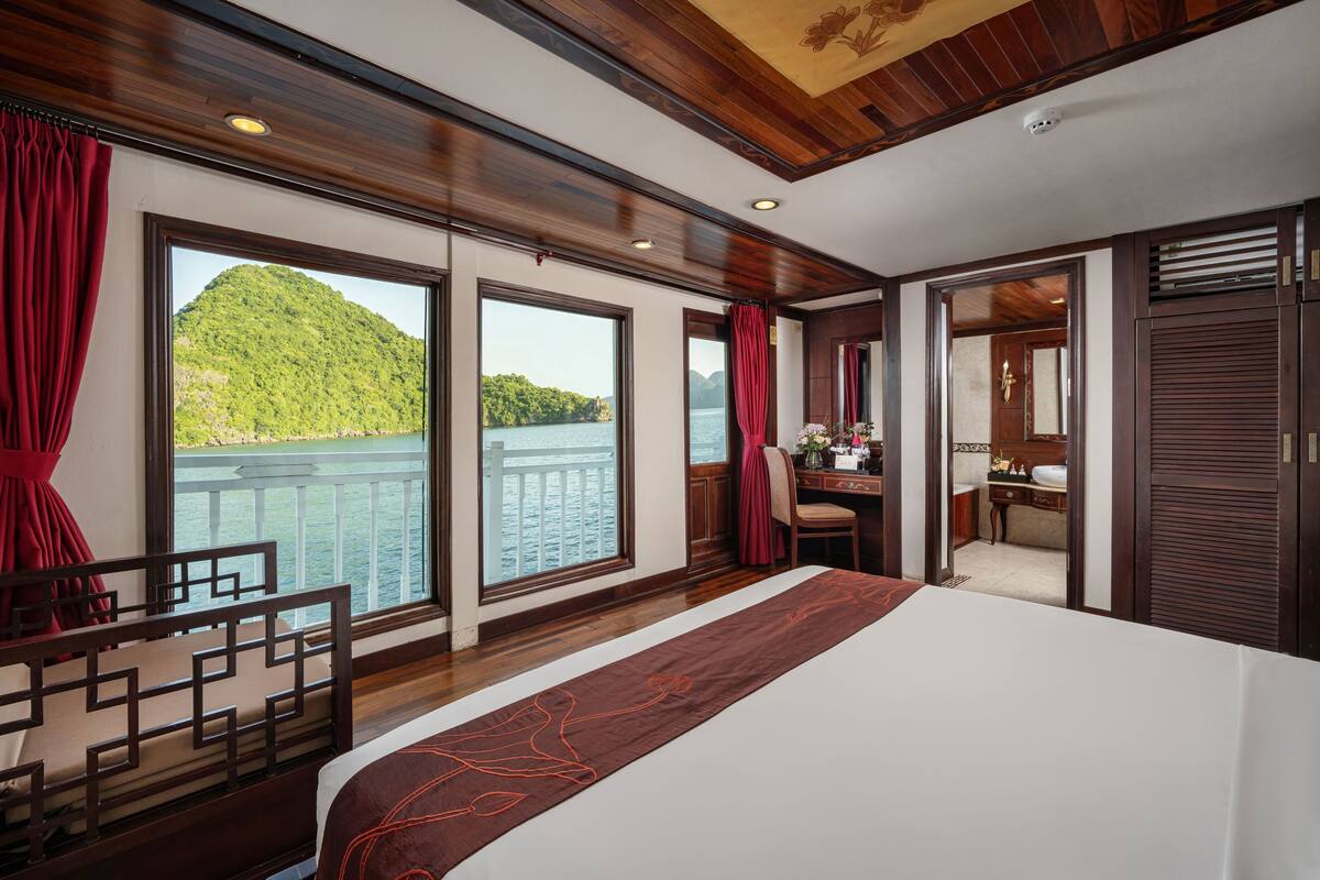 A room with a large bed, a desk, and a view of a lake and mountains.