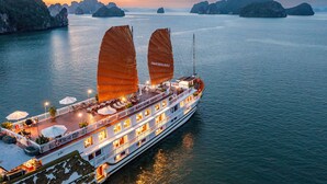 Een riviercruise schip met twee grote zeilen, een dek met terrasstoelen en uitzicht op het omliggende water en eilanden.