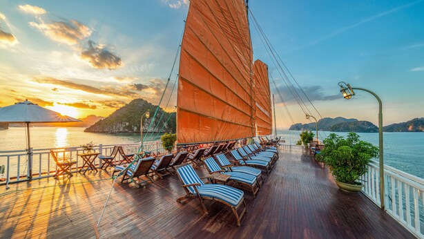 Een terras met lounge stoelen en een zeilboot met grote zeilen, met uitzicht op een waterpartij en verre eilanden.