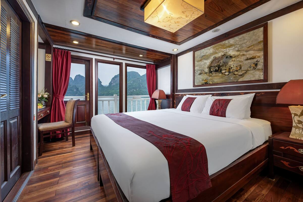 A hotel room with a large bed, wooden flooring, a desk with a chair, a nightstand, and a painting on the wall.