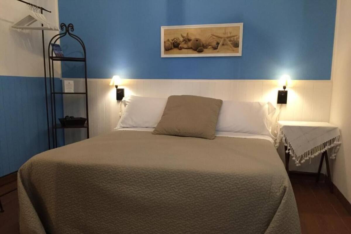 A bedroom with a large bed, two bedside tables, a wall-mounted shelf, and a painting.
