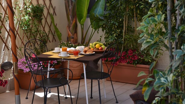 An outdoor patio with a table set for breakfast, surrounded by potted plants and a lattice wall. - Possidonea 28 Bed & Breakfast (Reggio Calabria)