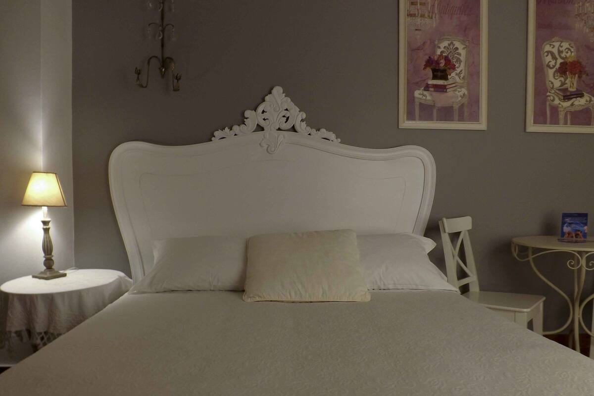 A neatly made bed with a white headboard, a bedside table with a lamp, and two framed pictures on the wall.