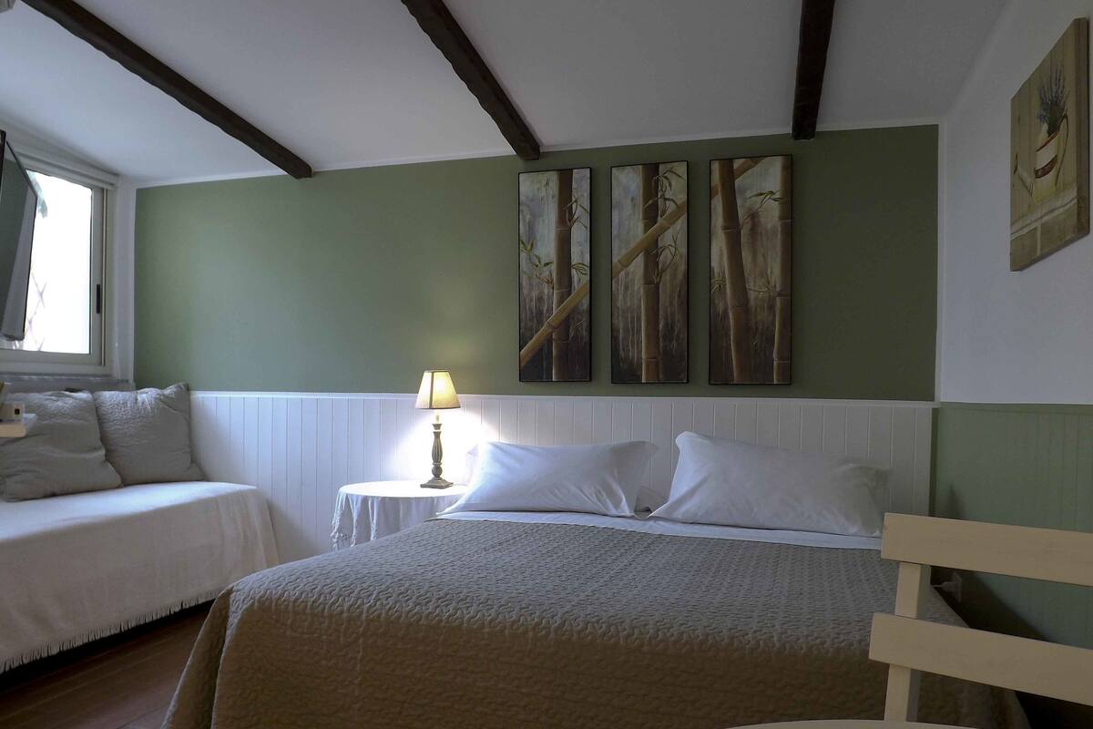 A bedroom with a bed, a bedside table with a lamp, and a window.