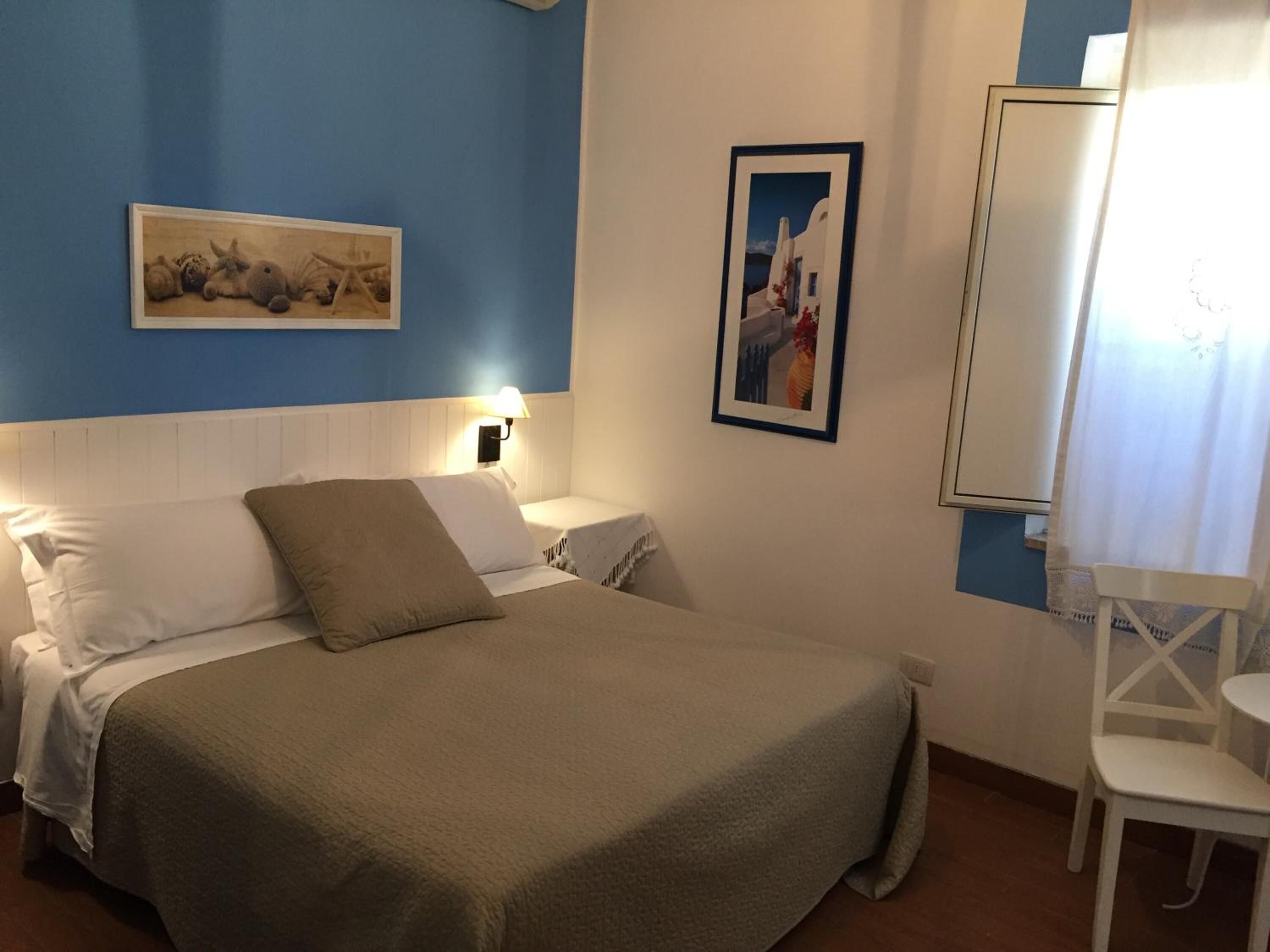 Un dormitorio con una cama, una mesita de noche, una silla y dos cuadros en la pared.