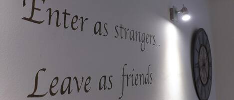 A wall with the text "Enter as strangers. Leave as friends." and a clock.